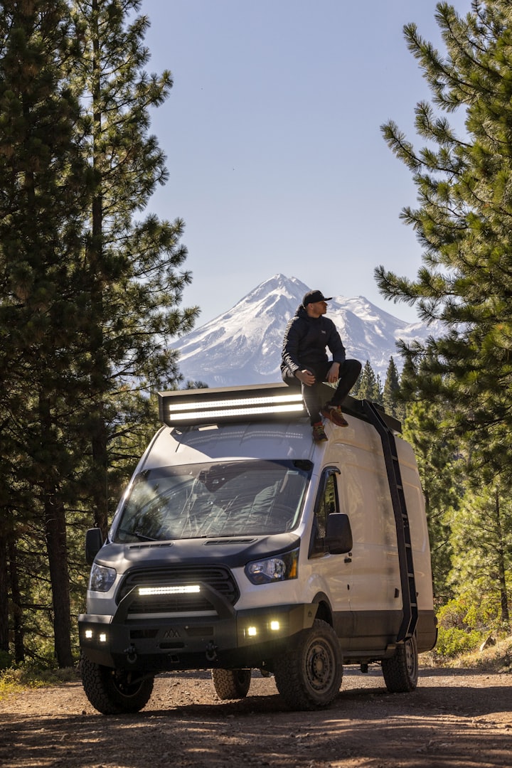 a man sitting on top of a van in the woods